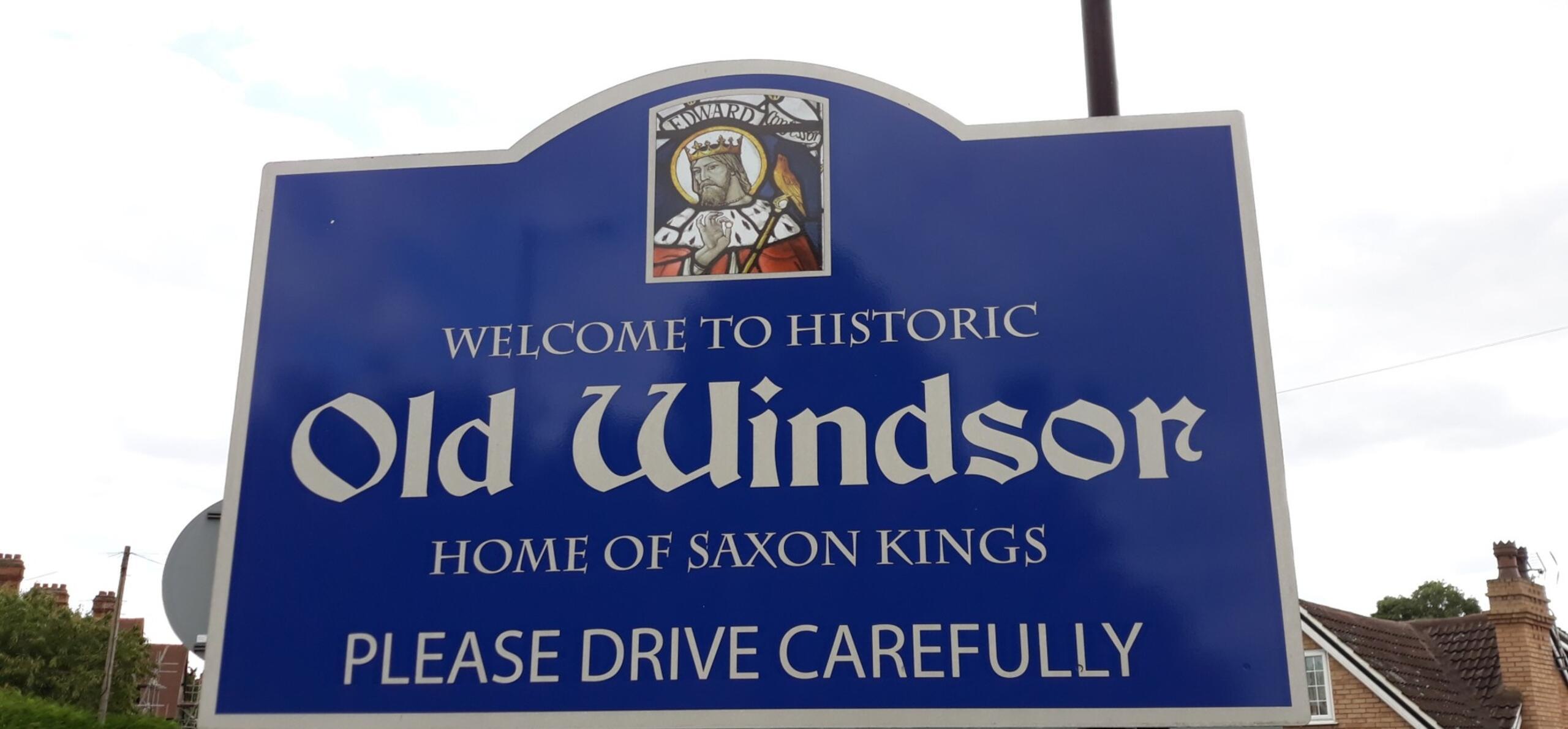 Photograph of a dark blue sign saying 'welcome to historic Old Windsor home of Saxon Kings, please drive carefully'